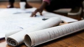 A persons hand pointing at a plan on a desk